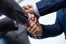 Create a modern, professional hero image for a webinar about growing small businesses through corporate sponsorships and partnerships with big corporations. Concept: diverse small business owners shaking hands with corporate executives across a table with subtle partnership documents, sponsor logos placeholders (generic, no real brands), and an upward growth chart in the background. Style: clean corporate, high-end, optimistic, minimal, soft depth of field, natural lighting. Color palette: white, charcoal, and a bold accent red similar to #E43B2C. Composition: centered, suitable for a circular crop (leave safe space around the main subjects), no text, no watermarks, no copyrighted logos.